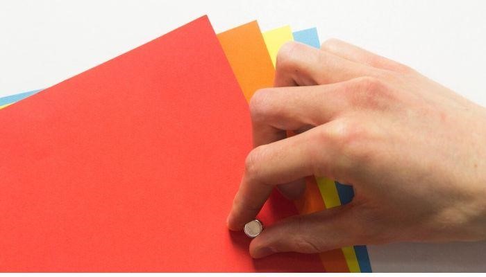 Slika roke kako pritrjuje barvne liste z magnetom na magnetno tapeto