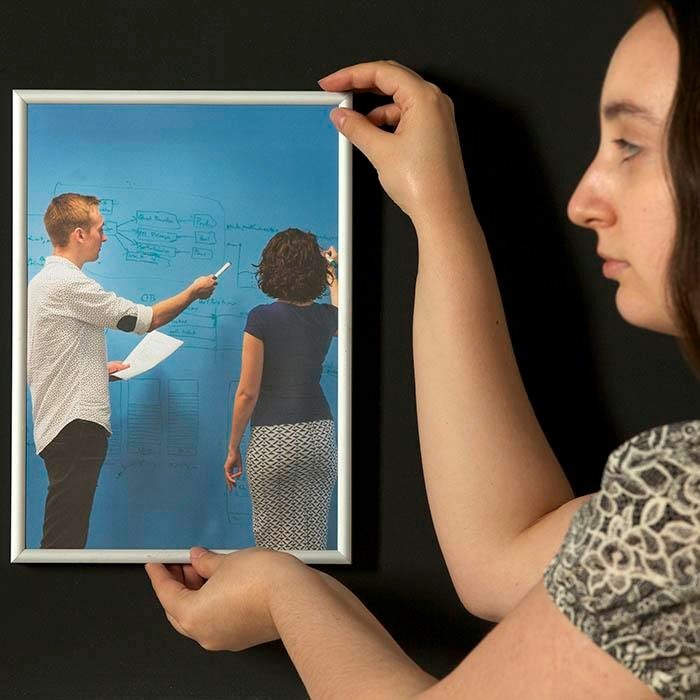 Ženska pritrjuje sliko z okvirjem na magnetno steno.